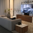 Ein graues Sofa vor einem Fernseher, darüber steht Lancia...