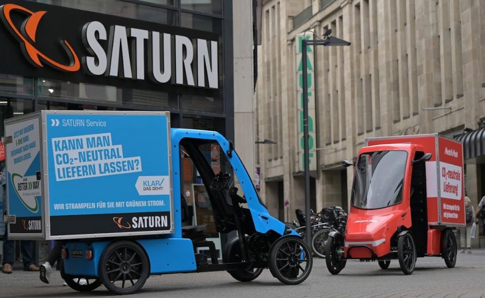 ein rotes und ein blaues e-Cargobike stehen vor einer Saturn-Filiale...