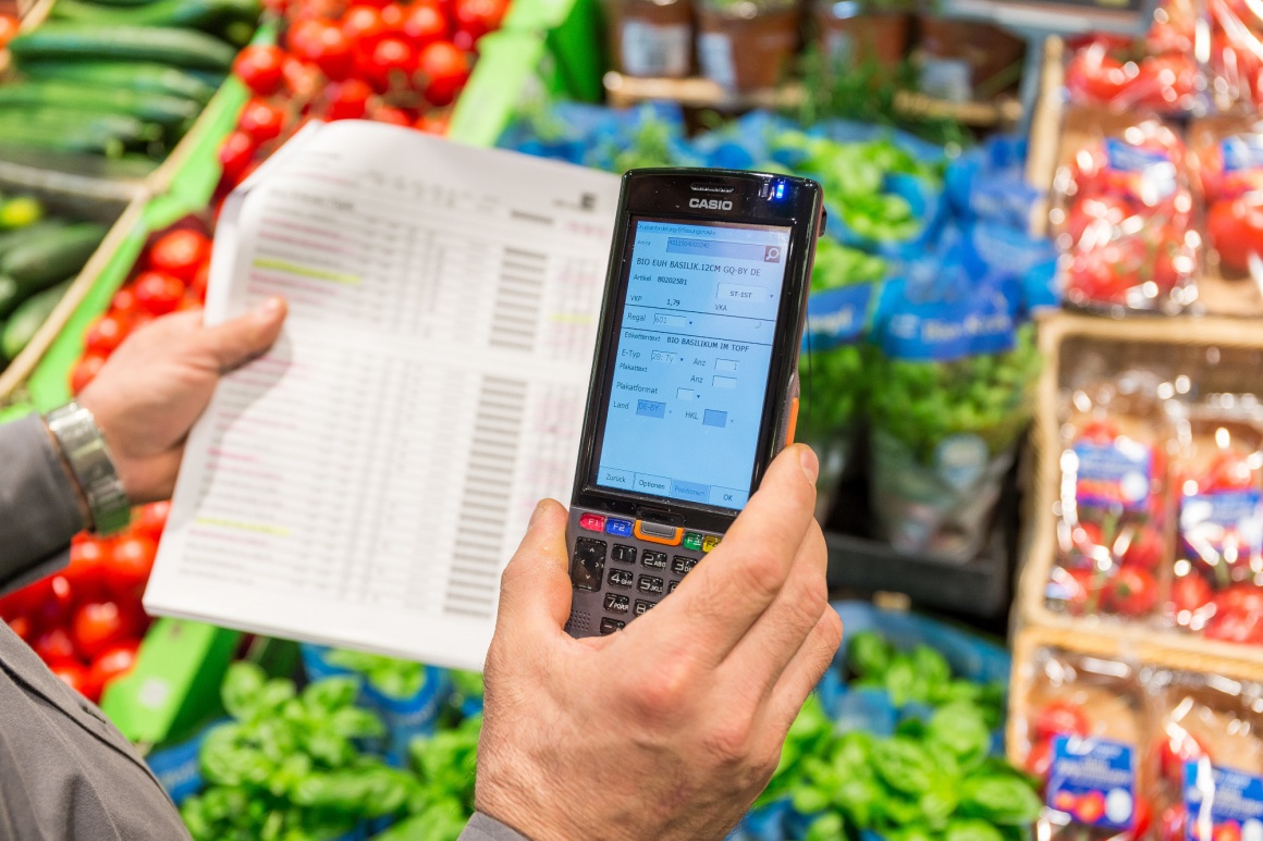 Eine Person steht in einer Gemüseabteilung und hält einen Warenscanner in der...