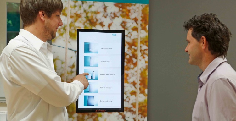 Foto: Zwei Männer vor einem digitalen Informationsbildschirm mit Produkten;...