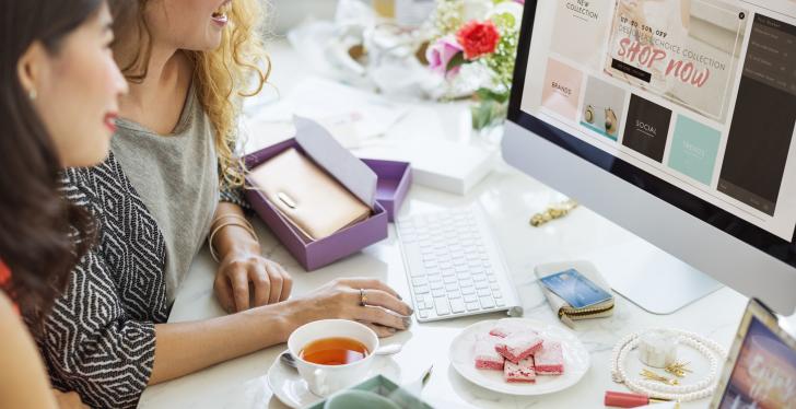 2 Frauen schauen auf einen Bildschirm, wo ein Webshop offen ist;...