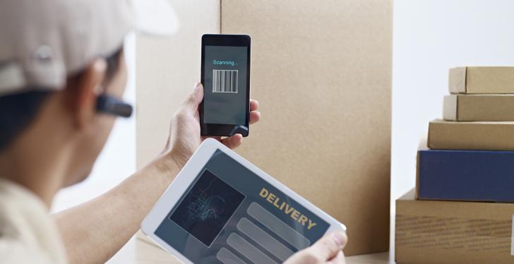 Logistikmitarbeiter scannt ein Paket mit Smartphone und hält Tablet in der...