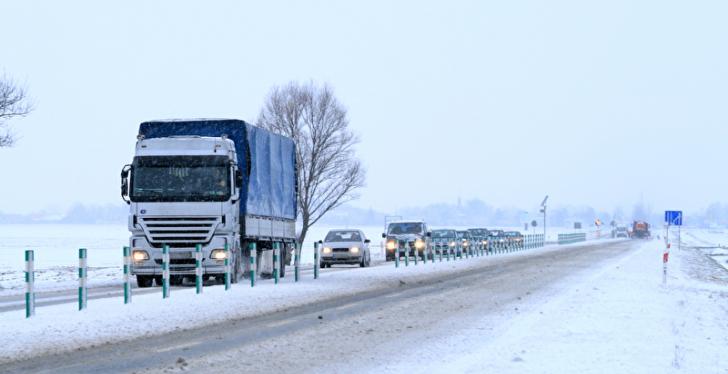 Lastwagen und Autos auf einer Landstraße in einer verschneiten winterlandschaft...
