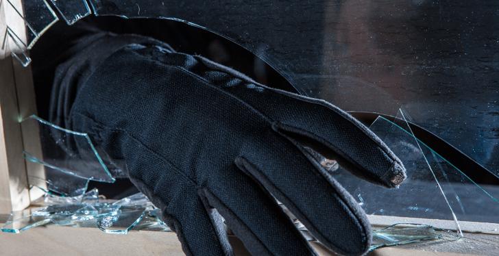 Einbrecher greift mit Hand in schwarzem Handschuh durch zerbrochenes Fenster...
