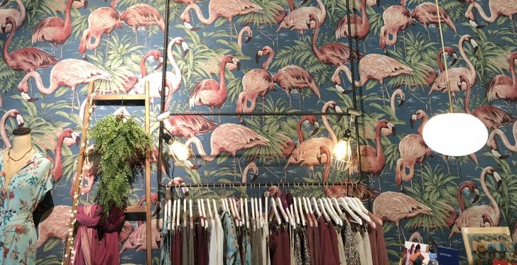 Eine Wand mit einer Flamingo-Tapete; davor: ein Kleiderständer mit bunten...