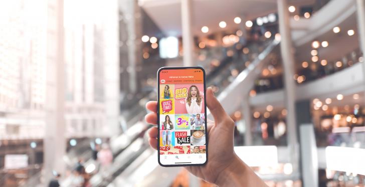 Hand hält Smartphone in Shoppingmall in die Höhe