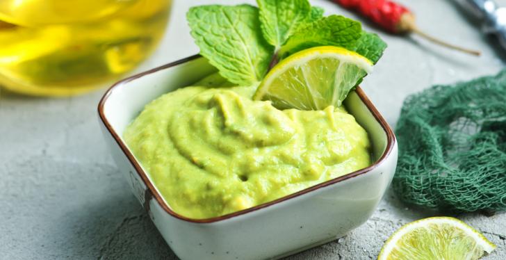 Eine viereckige weiße Schale mit grüner Guacamole, dekoriert mit einer...
