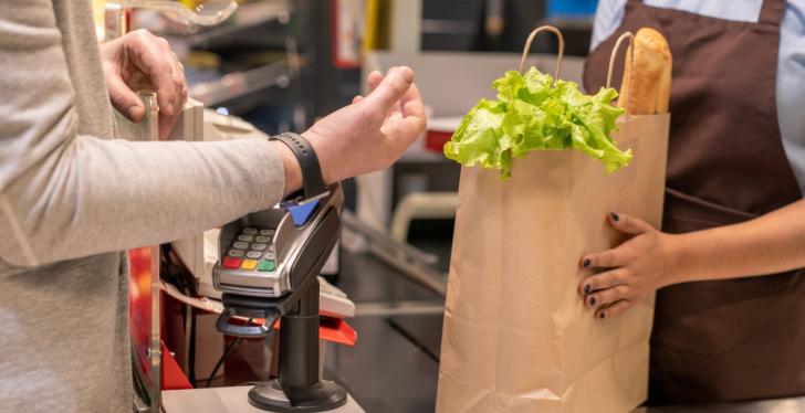 Ein Mann hält eine Smartwatch zum Bezahlen an ein Bezahlterminal im Supermarkt...