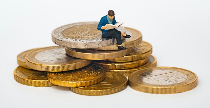 Eine winzige Plastikfigur sitzt auf mehreren Euro-Münzen...
