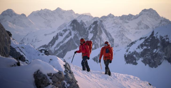 Zwei Personen mit roten Jacken in einem mit Schnee bedeckten Gebirge...