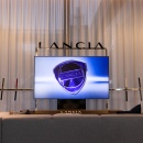 Ein graues Sofa vor einem Fernseher, darüber steht Lancia...