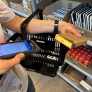 Person hält Produkt und Scanner, Warenkorb wird mit ausgewählten Artikeln...
