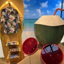 Sandruktur mit Sonnenbrille und Kokusnuss, im Hintergrund gelbe Badelatsche als...