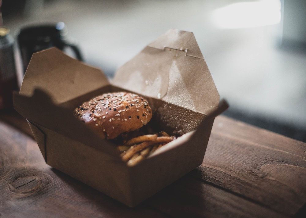 Eine Pappverpackung mit Burger und Pommes drin auf einem Holztisch...