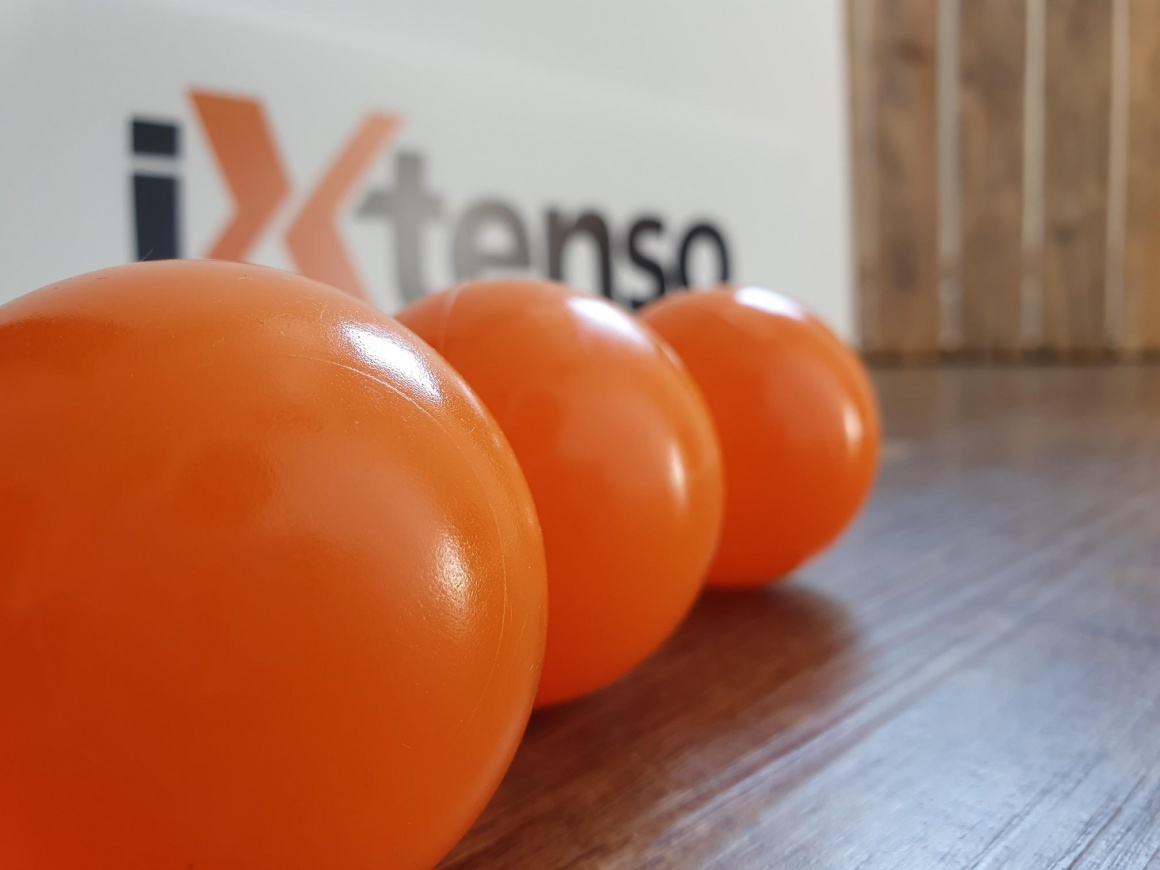 Drei orange-rote Bälle vor einem iXtenso-Schild