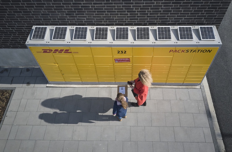 Eine DHL-Packstation mit Solarpanels auf dem Dach von oben fotografiert, davor...
