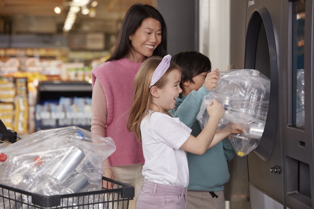 Eine Frau und zwei Kinder geben Leergut in Säcken an einem Automaten zurück;...
