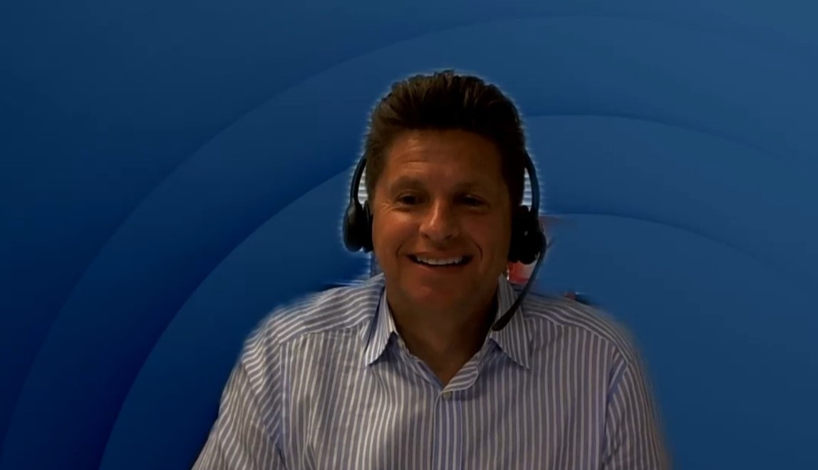 Ein Mann mit Kopfhörern und Mikrofon bei einem Webtalk vor einem blauen...