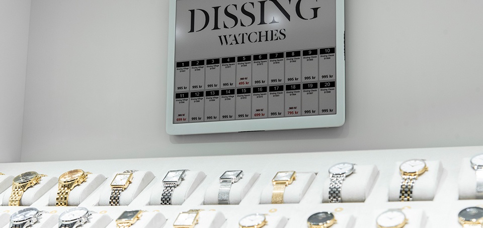 Eine Auswahl an hochwertigen Uhren. Darüber hängt ein ein großes digitales...