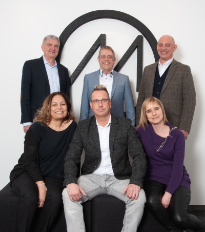 Sechs Personen in zwei Reihen stehen oder sitzen vor dem Molto-Luce-Logo...