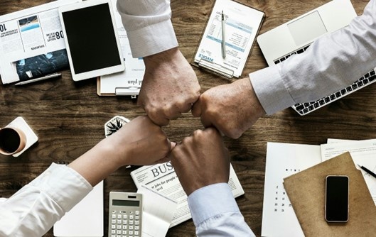 Vier Fäuste treffen sich zum Fistbump über einem Schreibtisch mit Dokumenten,...