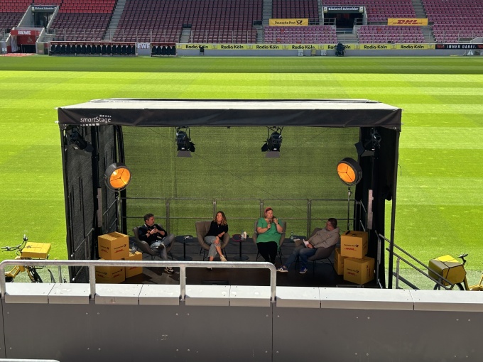 Eine Bühne im RheinEnergieSTADION. Auf der Bühne findet ein reger Austausch...