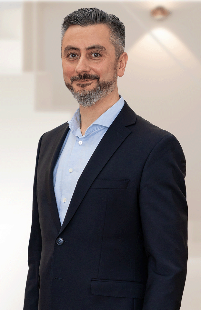 Mann in dunklem Anzug mit hellblauem Hemd steht seitlich und achaut in die...