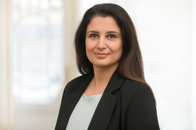 Frau mit dunklen offenen Haaren und in schwarzem Blazer lächelt in die Kamera...