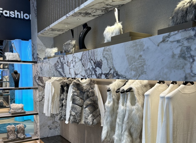 Kleiderstange mit grauweißer, hochwertig wirkender Kleidung vor Mamorwand....