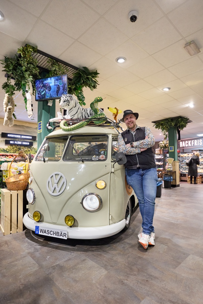 Mann mit Hut lehnt in einer Filiale an einem alten VW-Bus...