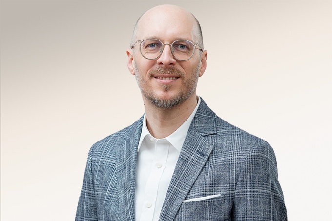 Mann mit kurzen Haaren und Brille und kariertem Jacket lächelt in die KAmera...