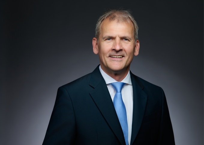 mann in dunklem Anzug mit weißem Hemd und hellblauer Krawatte lächelt in die...