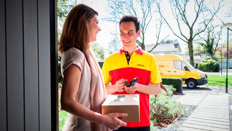 Frau nimmt in der Tür Paket von DHL-Boten an