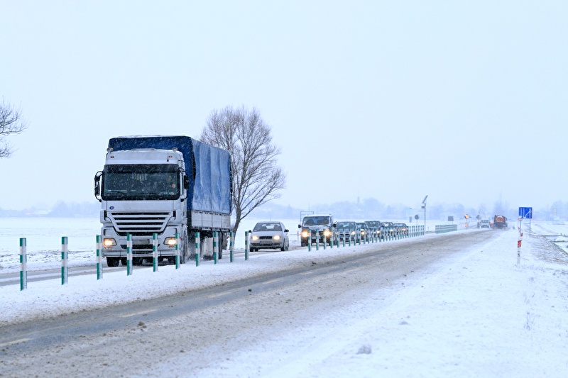 Lastwagen und Autos auf einer Landstraße in einer verschneiten winterlandschaft...