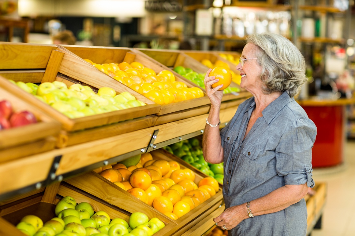 Ältere frau steht vor Obstregal im Supermarkt und riecht an Orange...