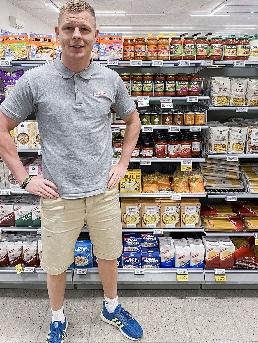 Ein junger Mann steht in einem kleinen Laden vor einem Lebensmittelregal...