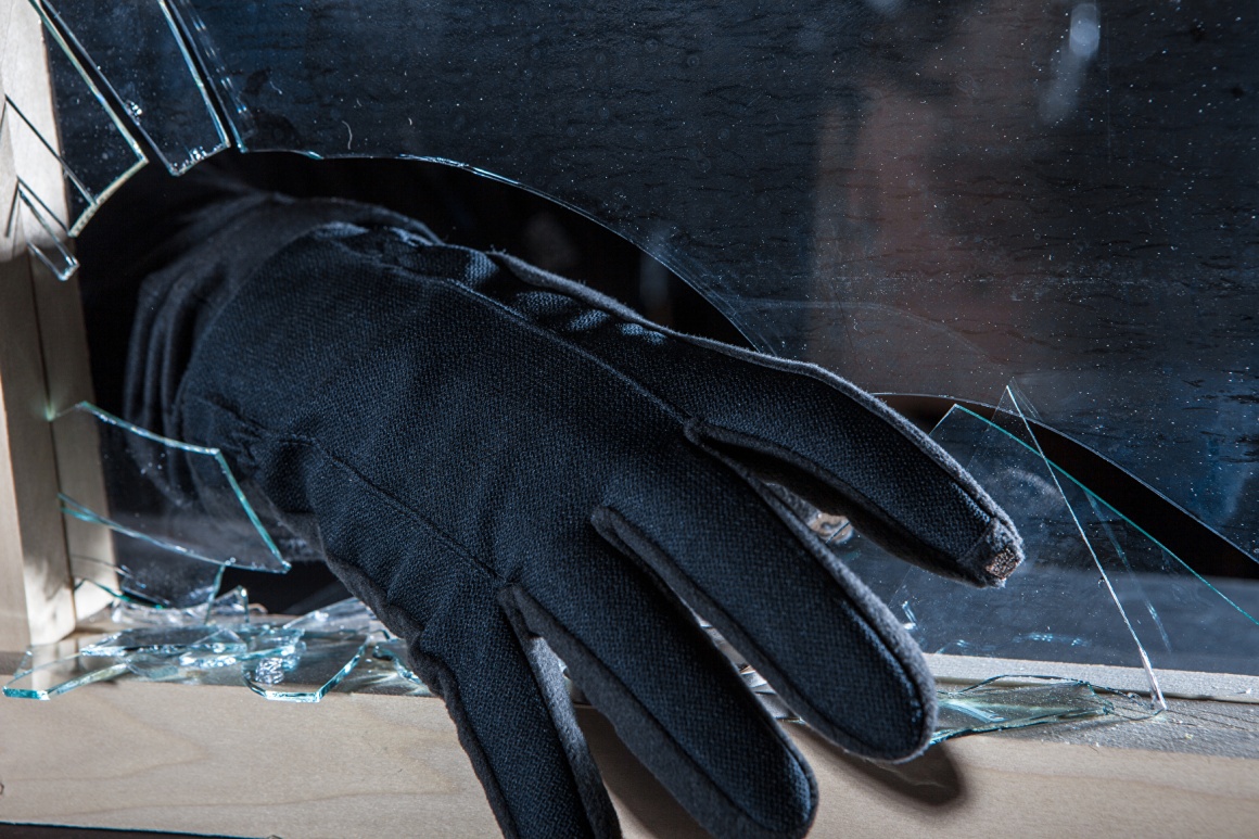 Einbrecher greift mit Hand in schwarzem Handschuh durch ein zerbrochenes Fenster...