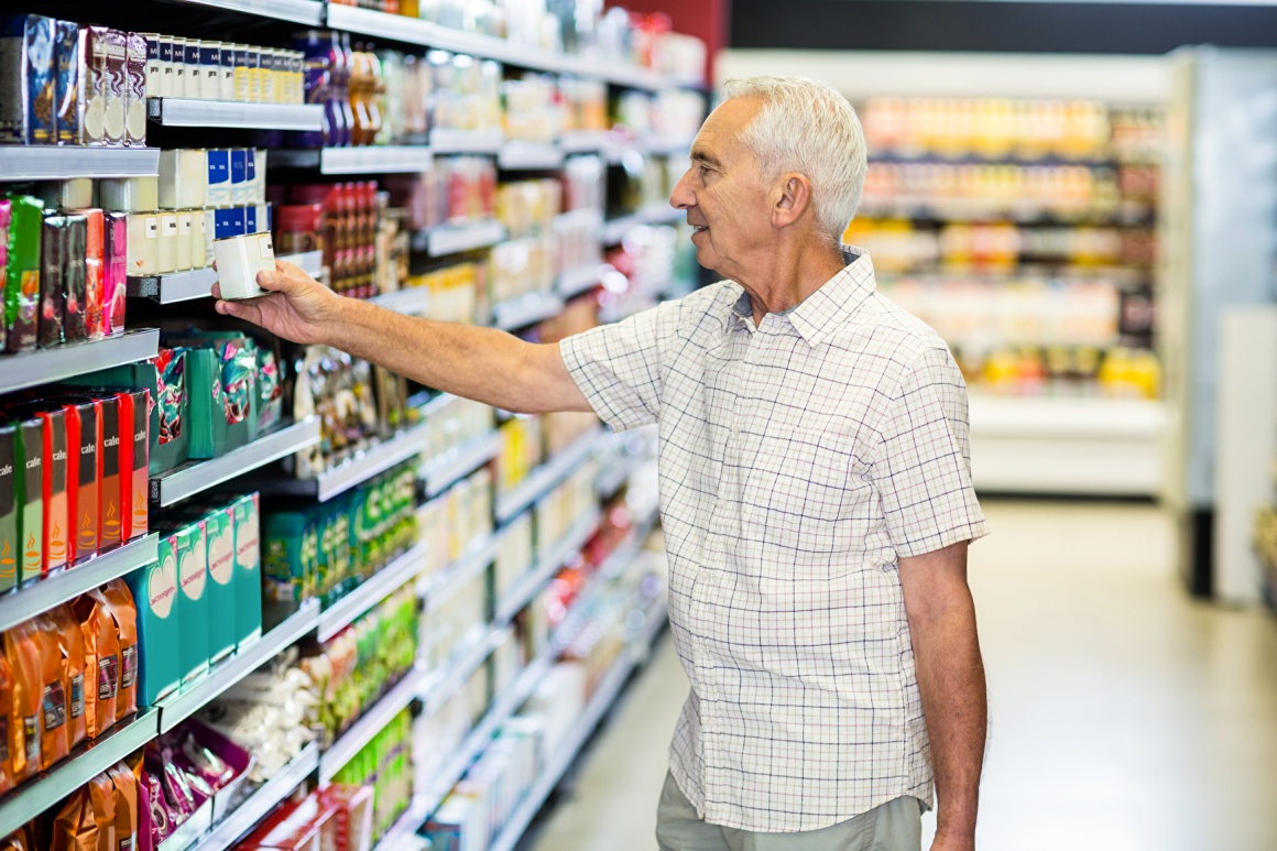 Älterer Mann greift nach einem Produkt im Supermarktregal...