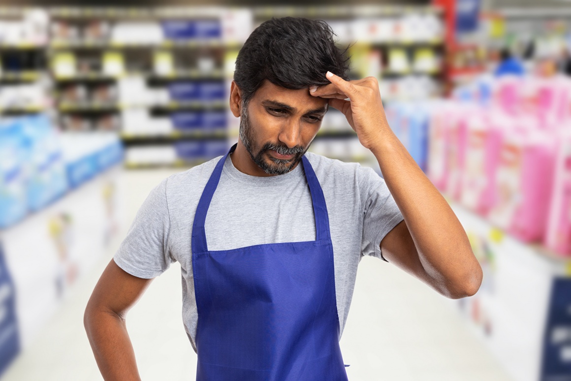 Ein männlicher Supermarktangestellter berührt sich mit der Hand die Stirn...