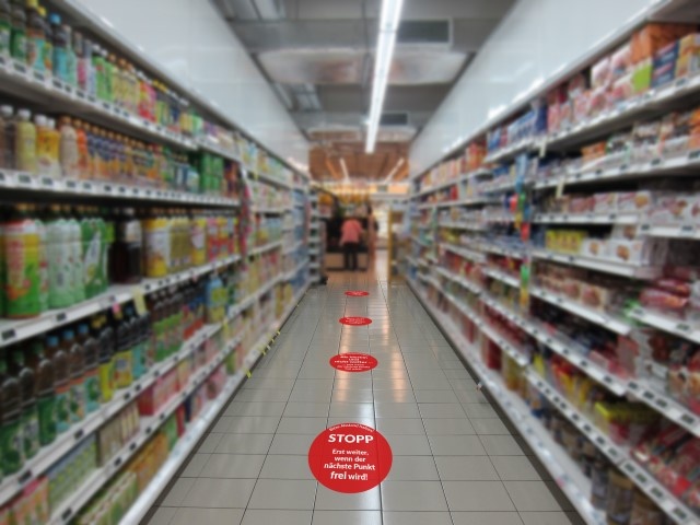 Rote Punkte auf dem Boden eines Supermarkts markieren den Mindestabstand...