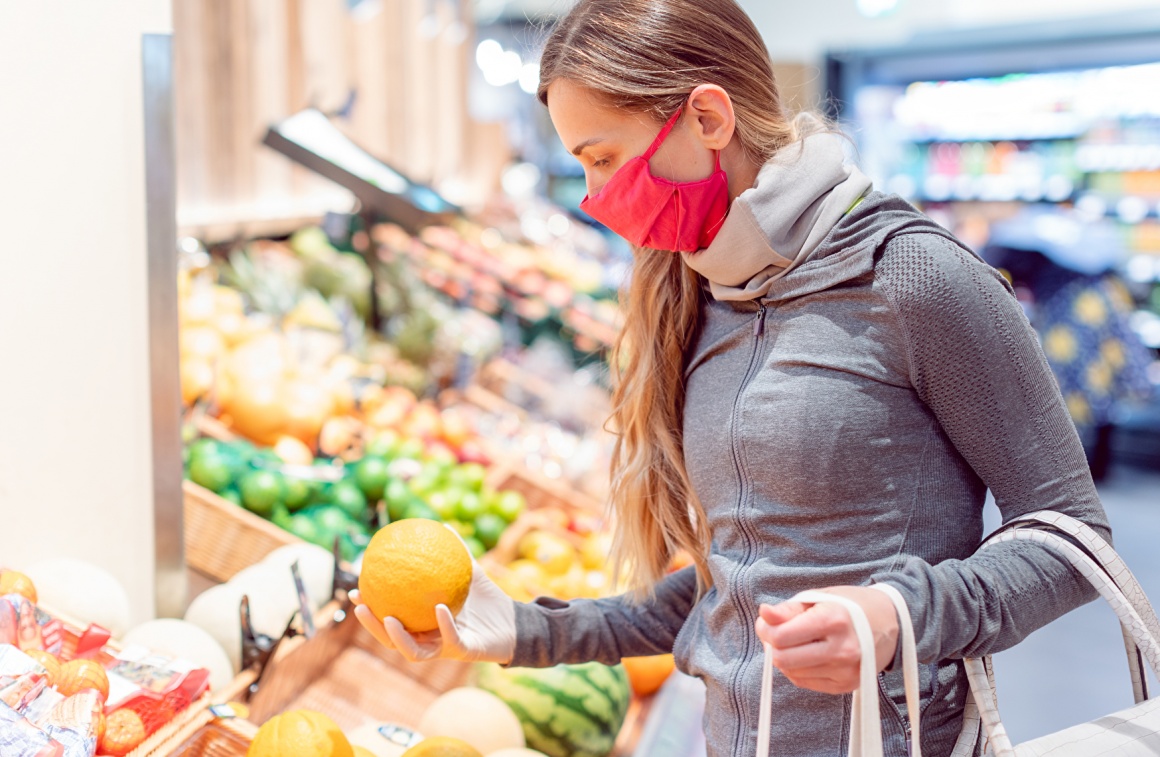 Frau mit Mundschutz und Handschuhen in der Gemüseabteilung im Supermarkt...