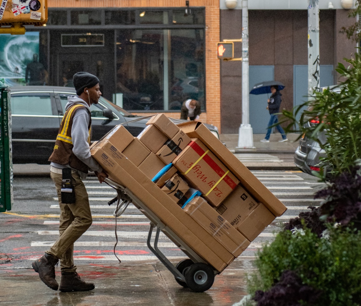 Ein Paketdienstmitarbeiter fährt eine Karre mit sehr vielen Paketen auf einer...
