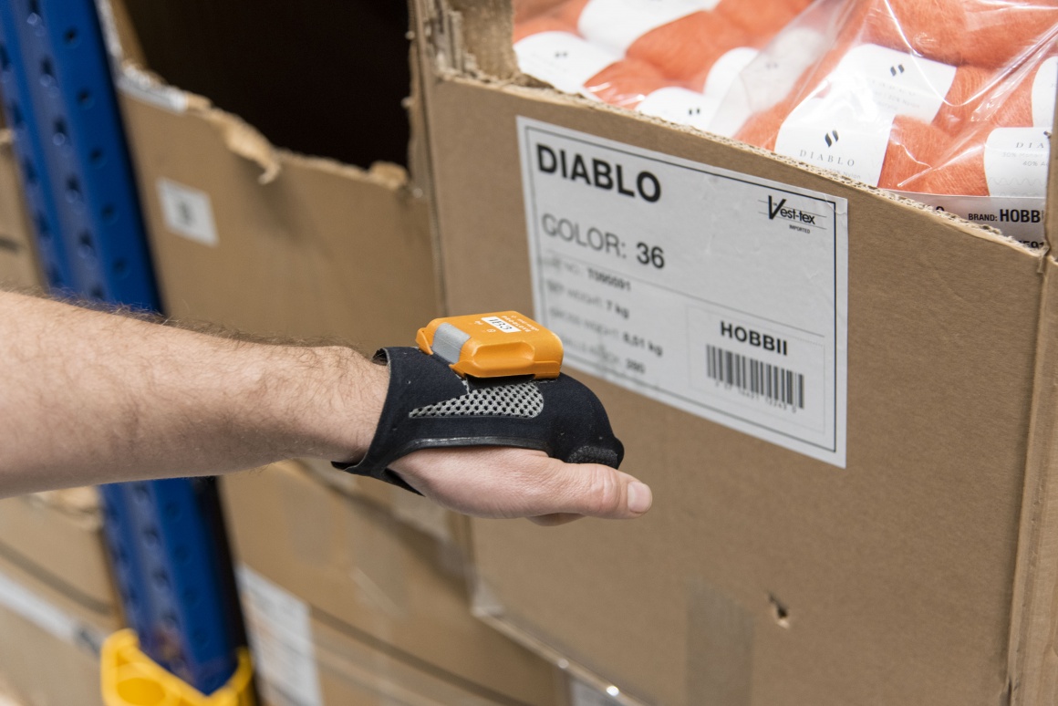 Shows the hand of a worker scanning a product package with a hands-free scanner...