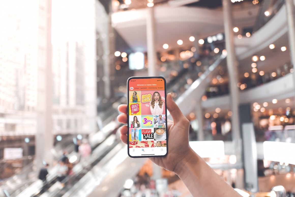 Hand hält Smartphone in Shoppingmall in die Höhe