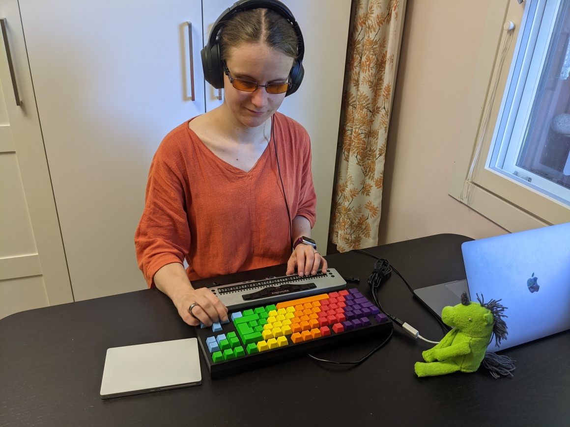 Blinde Frau sitzt vor einer bunten Tastatur und einem Screenreader...