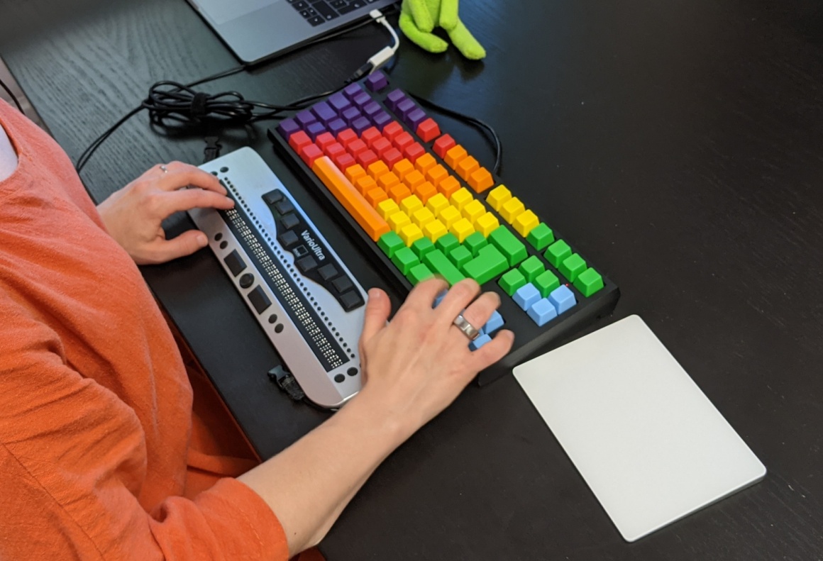 Detailaufnahme: Blinde Frau sitzt vor einer bunten Tastatur und einem...