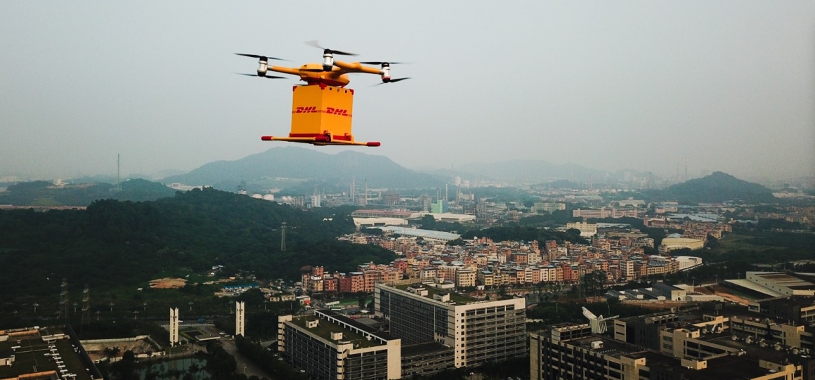 Eine gelbe DHL-Drohne fliegt hoch über einer Stadt...