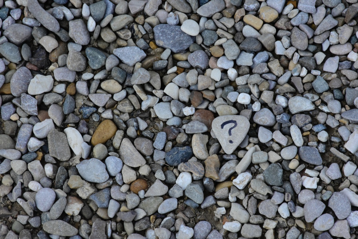 Viele kleine Steine, ein Stein davon mit einem aufgemalten Fragezeichen...