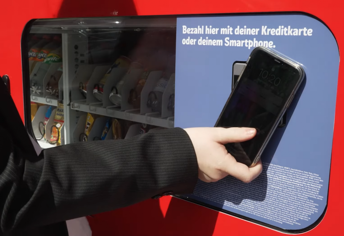 Eine Person hält ein Smartphone an den selbstfahrenden Kiosk um zu bezahlen...